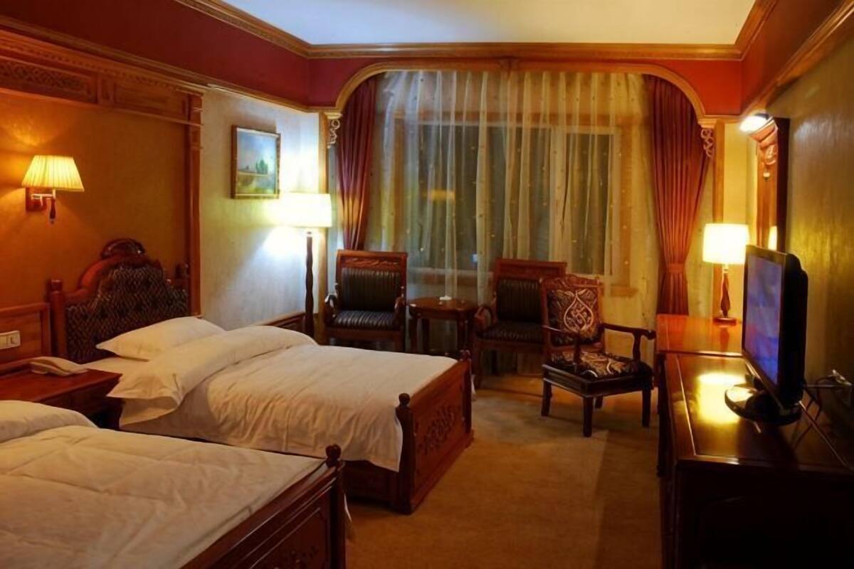 Een hotelkamer met twee bedden, een bureau, een stoel, een televisie en een raam met gordijnen.