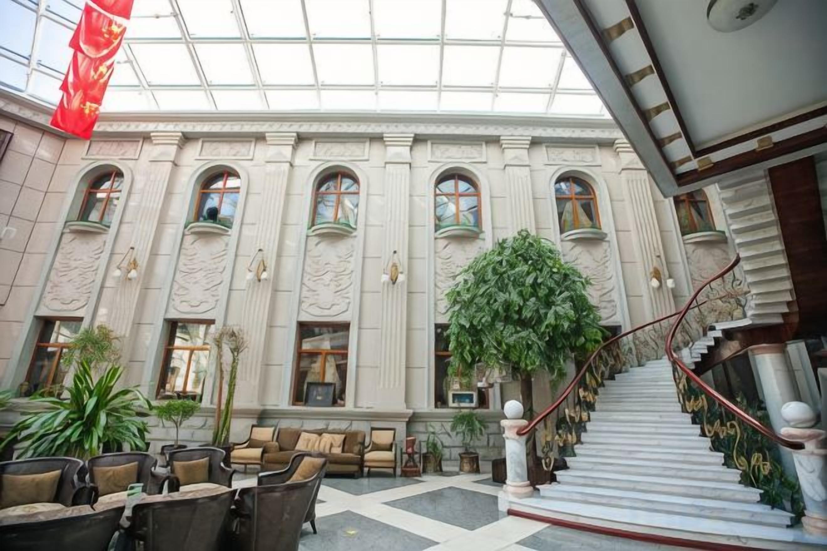 A spacious lobby with a grand staircase, multiple seating areas, and a large indoor plant.