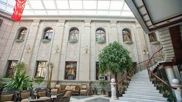 A spacious lobby with a grand staircase, multiple seating areas, and a large indoor plant.