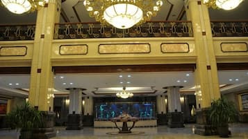 A spacious lobby with a grand chandelier, a reception desk, and a large aquarium.