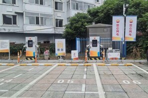 Un área de estacionamiento con espacios numerados, un edificio con múltiples ventanas y una reja azul.