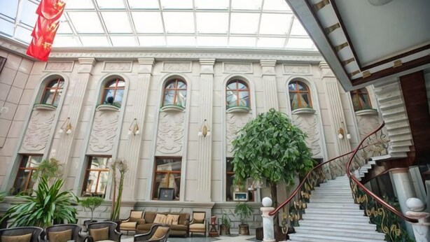 Un vestíbulo de hotel con una escalera monumental, varias zonas de estar y una gran planta de interior.
