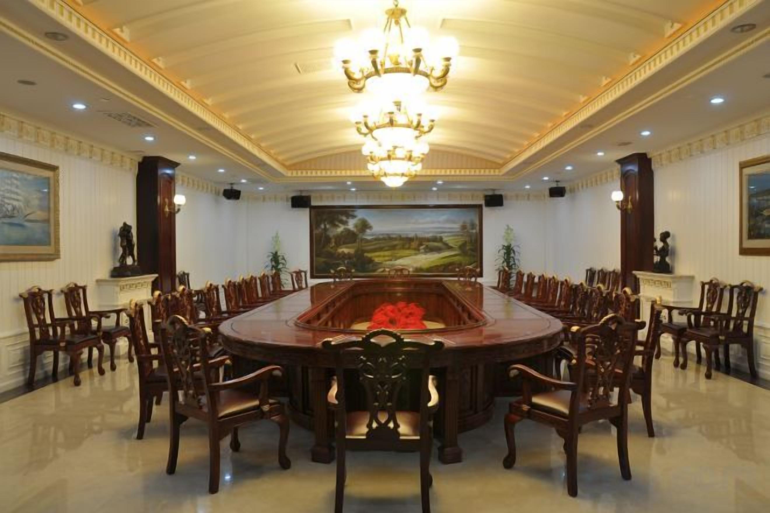 A formal meeting room with a large oval table, wooden chairs, a chandelier, and paintings on the walls.