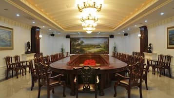 A formal meeting room with a large oval table, wooden chairs, a chandelier, and paintings on the walls.