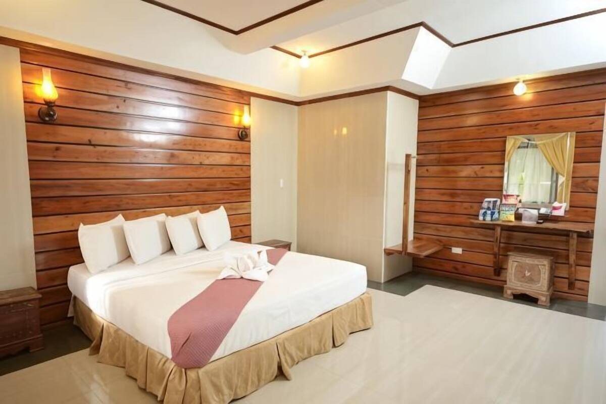 Une chambre à coucher avec une tête de lit en bois, un lit recouvert de draps blancs, une table de chevet et un miroir au-dessus de la commode.
