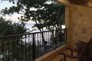 A balcony with a metal railing, a wooden bench, and a view of trees and a body of water.