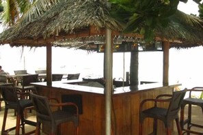 Een terras met een rieten dak, barstoelen en uitzicht op zee.