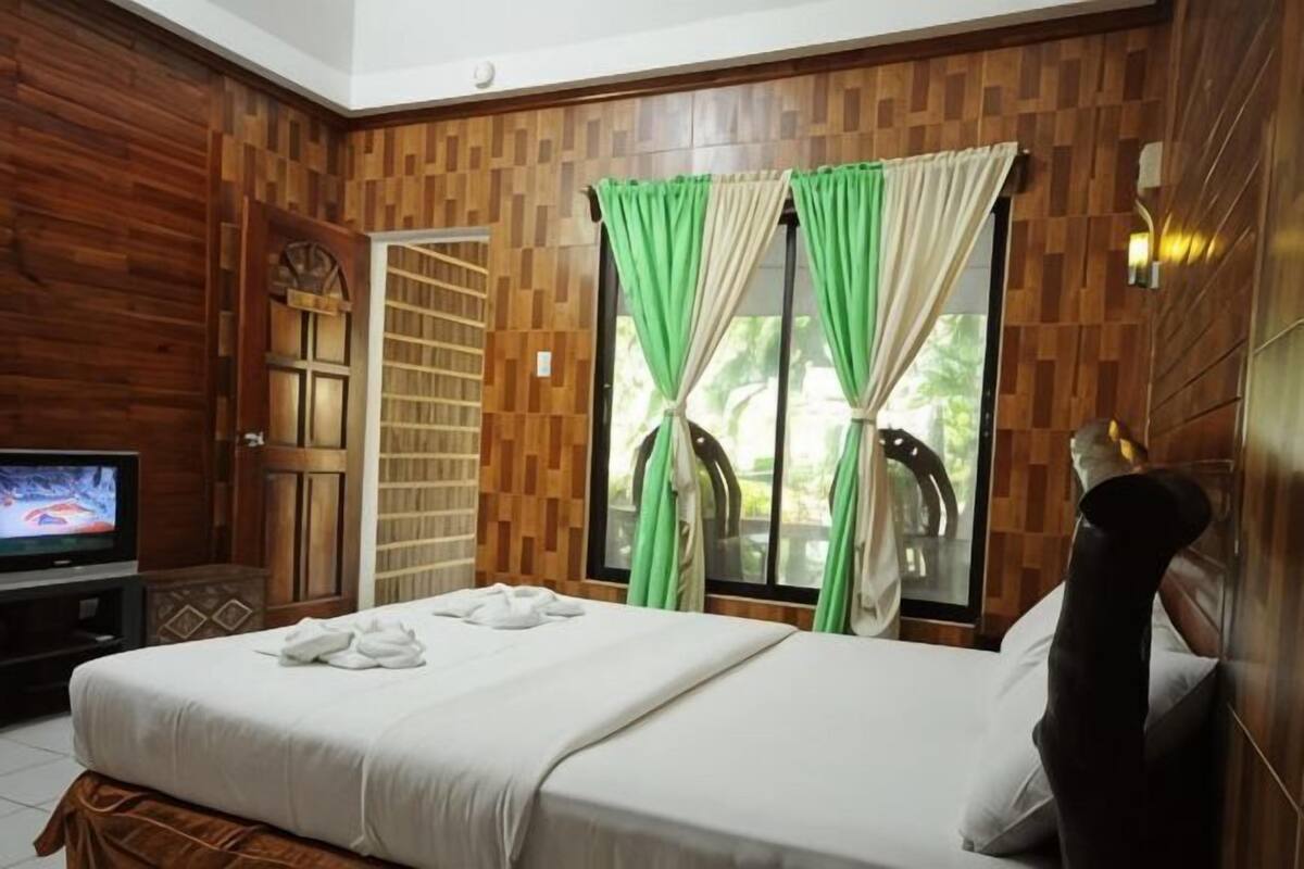 Une chambre à coucher avec un lit, un téléviseur, des lambris en bois et une fenêtre avec des rideaux.
