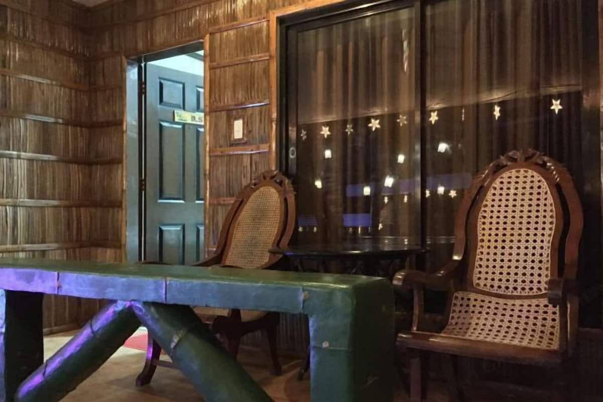 Une pièce aux murs en bois, avec un banc vert et deux fauteuils en osier.