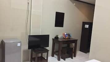 Een kleine kamer met een televisie, een bureau en een koelkast.
