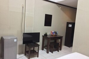 Een kleine kamer met een televisie, een bureau en een koelkast.