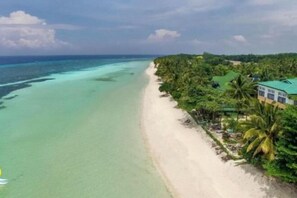 Une plage avec une eau turquoise et limpide, un rivage sablonneux et un bâtiment surmonté d’un toit végétalisé.