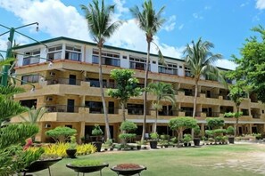 Um hotel com vários andares e varandas, rodeado por palmeiras e jardins bem cuidados.