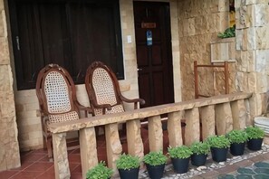Un bâtiment en pierre avec un banc en bois et deux chaises en osier devant.
