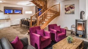 A modern living room with a wooden staircase, a fireplace, and a dining area with a kitchen in the background. - Residence Lipno by Interhome (Lipno nad Vltavou)