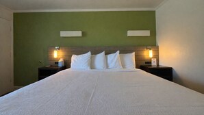 A hotel room with a large bed, green walls, and two bedside lamps. - Classic King Room - Sleeps 2 (Monterey)