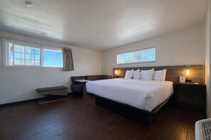 A bedroom with a large bed, a desk, a chair, and a window.