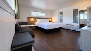A hotel room with a bed, a desk, a chair, a sofa, and a window with curtains. - Signature King Room - Larger Layout - Sleeps 2 (Monterey)