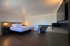 A hotel room with a bed, bedside tables, a sofa, a desk, and a flat-screen TV.