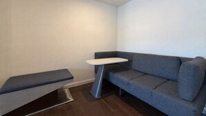 A corner room with a grey sofa, a small table, and a bench. - Deluxe 2 Queen Room - Extra Spacious Layout - Sleeps 4 (Monterey)