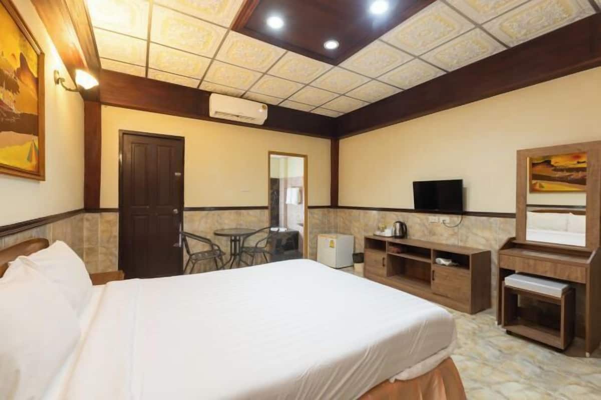 Quarto de hotel com cama, escrivaninha, cadeira, televisão, espelho e um pequeno frigorífico.