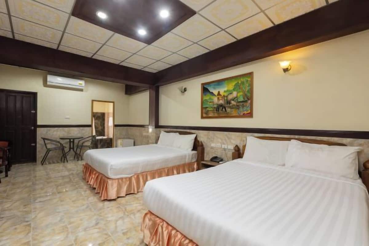 Quarto de hotel com duas camas, um quadro na parede, teto com iluminação embutida e piso ladrilhado.