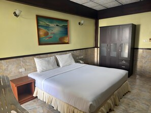 A hotel room with a bed, a nightstand, a wardrobe, and a painting of a beach scene. - Kata Palace Hotel (Phuket)