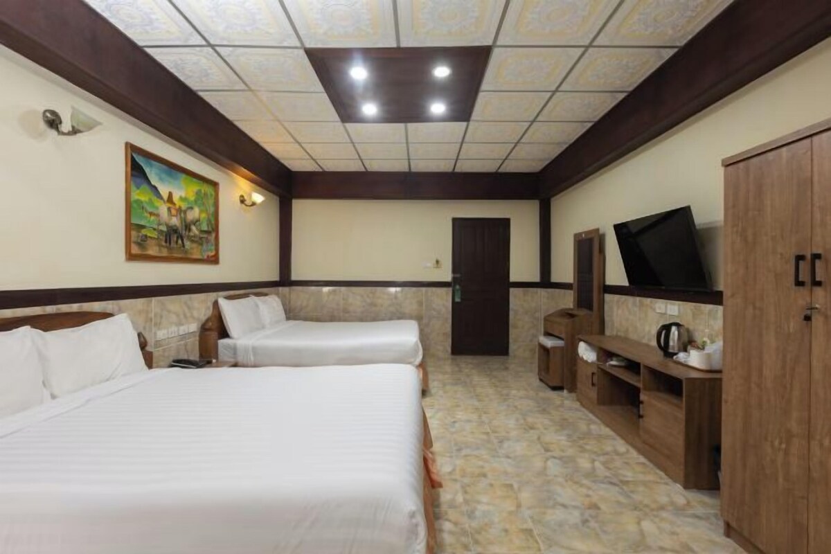 A hotel room with two beds, a television, a painting on the wall, and a tiled ceiling.