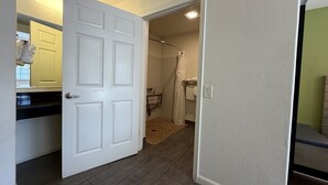 Een gang die leidt naar een badkamer met een douche, een handdoekrek en een deur met een handgreep.