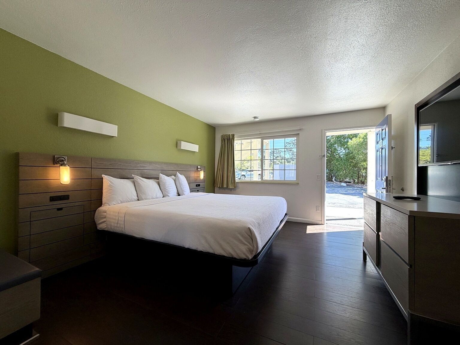 A hotel room with a bed, bedside tables, a TV, and a window with curtains.