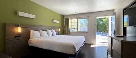 A hotel room with a bed, bedside tables, a TV, and a window with curtains.