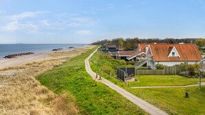 Une zone résidentielle côtière où les maisons se distinguent par leurs toits recouverts de tuiles rouges, une plage de sable fin et un ciel dégagé.