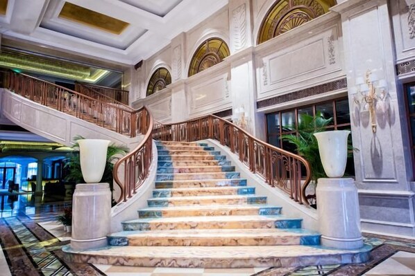 Un magnifique escalier en marbre, avec des marches de marbre et une rampe en bois, menant à l’étage supérieur.