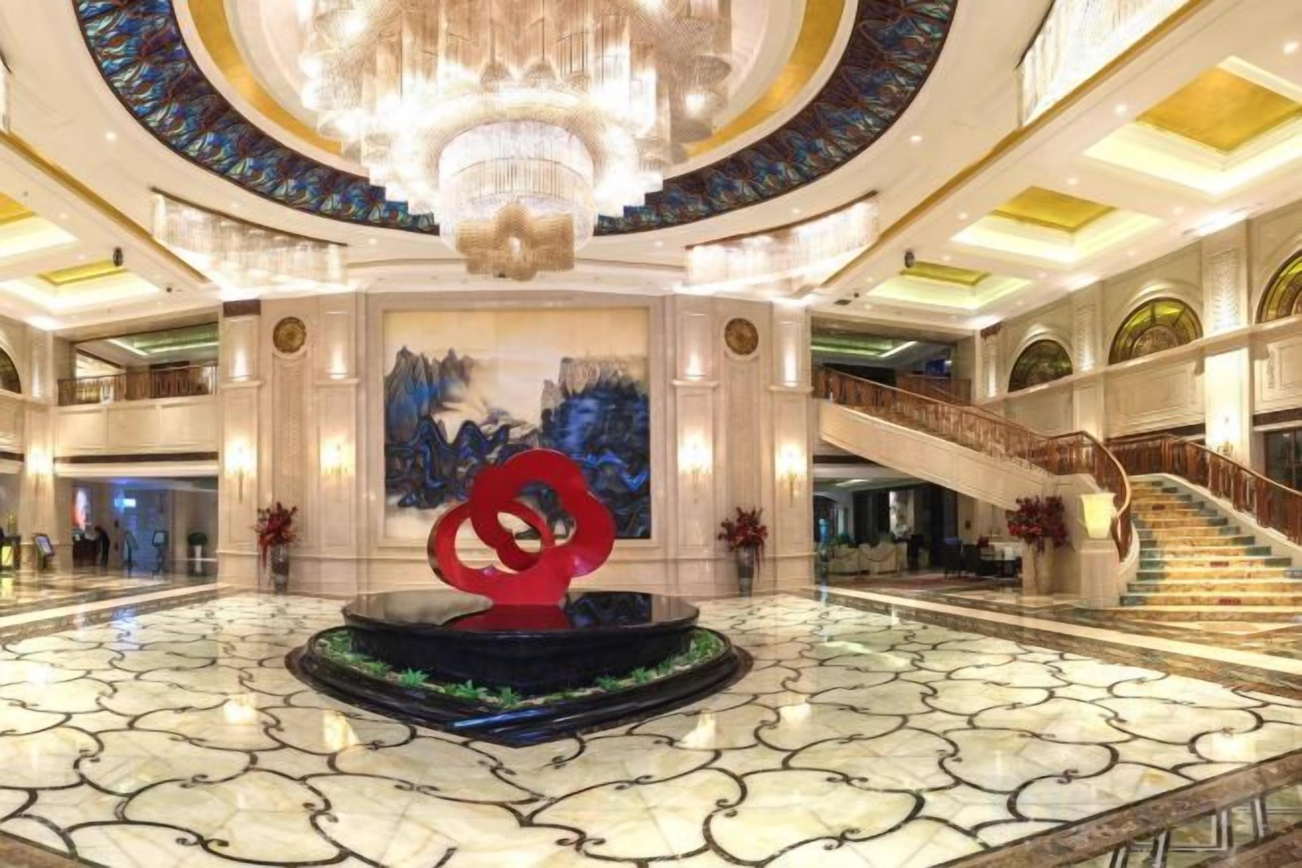 A spacious lobby with a central fountain, a grand staircase, and a chandelier.