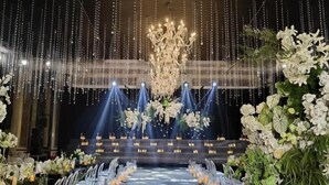 Une scène ornée d’un lustre, de compositions florales et de rangées de chaises.