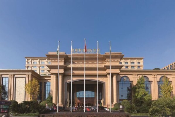 A large, classical building with a grand entrance, multiple flags, and a well-maintained garden in front. - Xingchen Hangdu International Hotel (Chengdu)