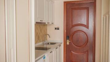 A compact kitchen with white cabinets, a stainless steel sink, and a wooden door.
