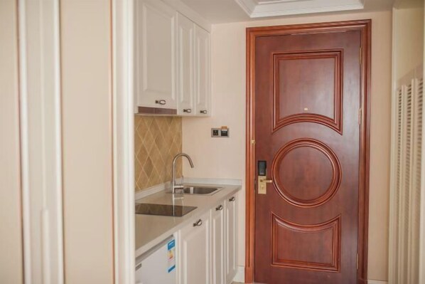 A compact kitchen with white cabinets, a stainless steel sink, and a wooden door. - Xingchen Hangdu International Hotel (Chengdu)