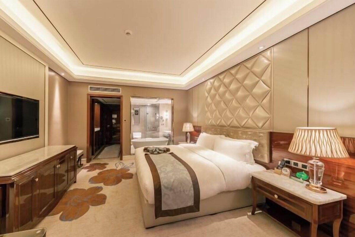 A hotel room with a large bed, a TV, a desk, and a bathroom visible through an open door.
