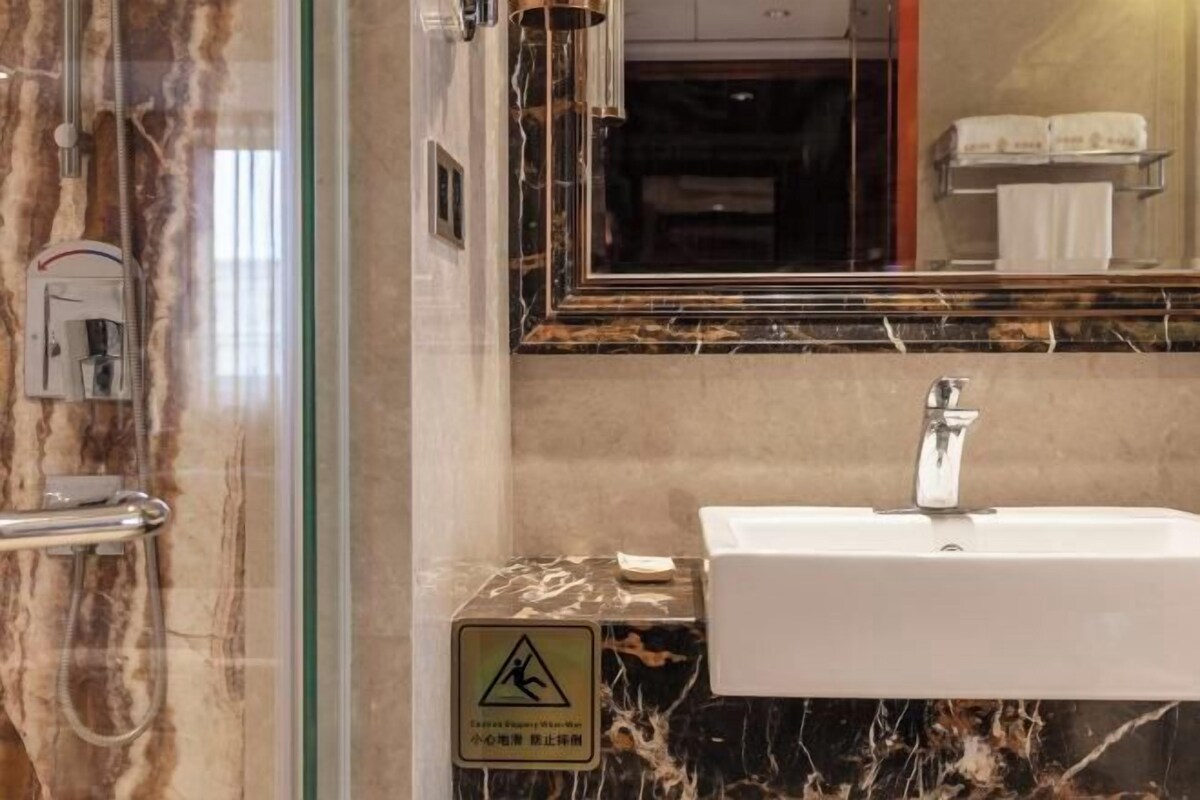 A bathroom with a marble sink, a glass shower enclosure, and a mirror reflecting a towel rack and a toilet paper holder.