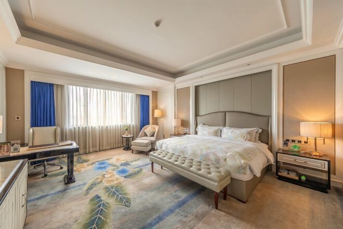 A hotel room with a large bed, a desk, a chair, and a nightstand with lamps.