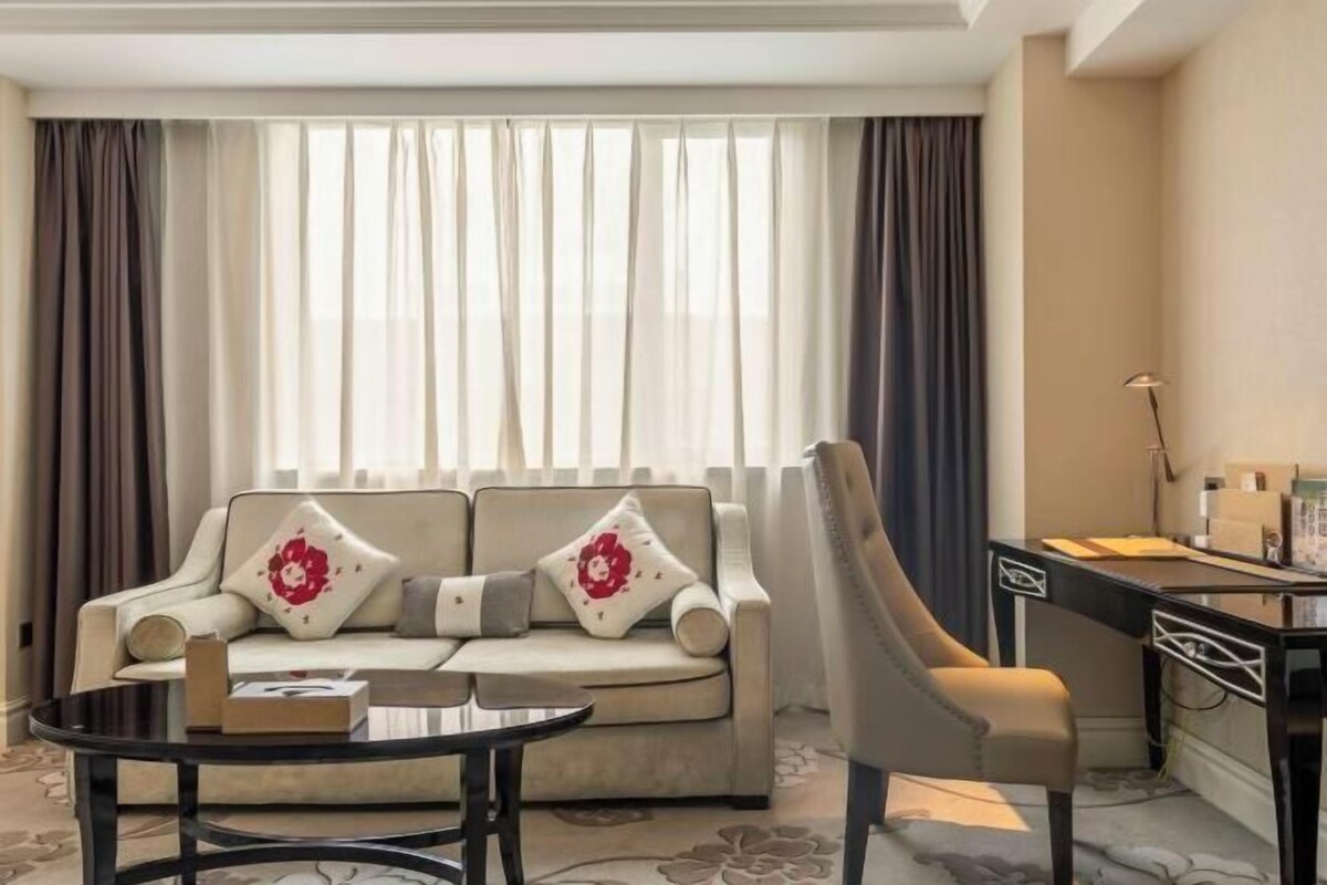 A hotel room with a sofa, a small table, a desk, and a lamp.