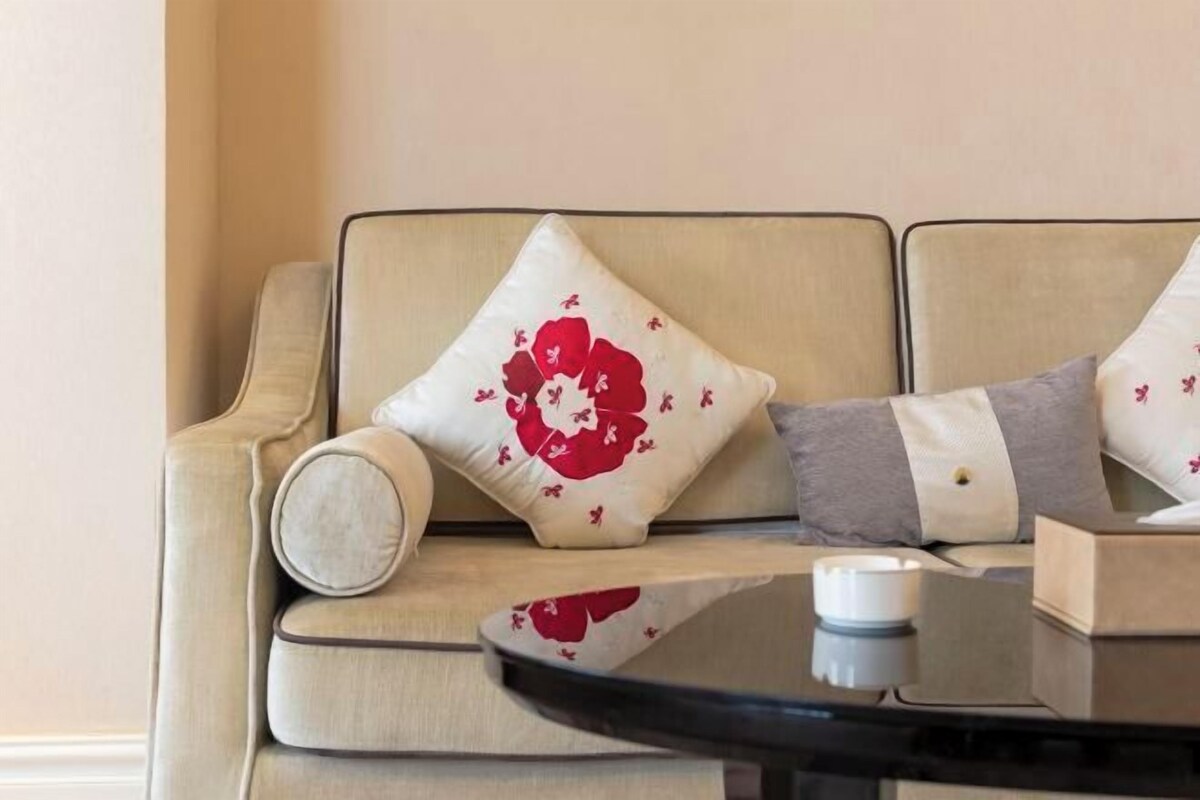 A beige sofa with floral-patterned cushions, a small table with a white candle, and a book.