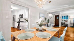 Un coin repas avec une table en bois, des chaises blanches et un lustre.