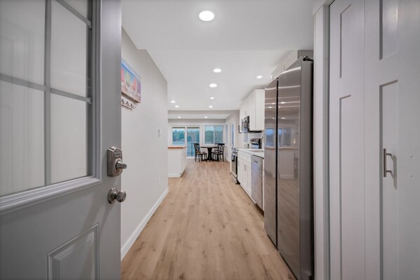 A modern kitchen with white cabinets, a stainless steel refrigerator, and a wooden floor.