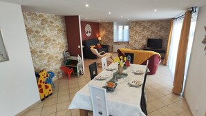 Una zona de menjador amb una taula per a quatre, un sofà, una televisió i una peça decorativa a la paret.