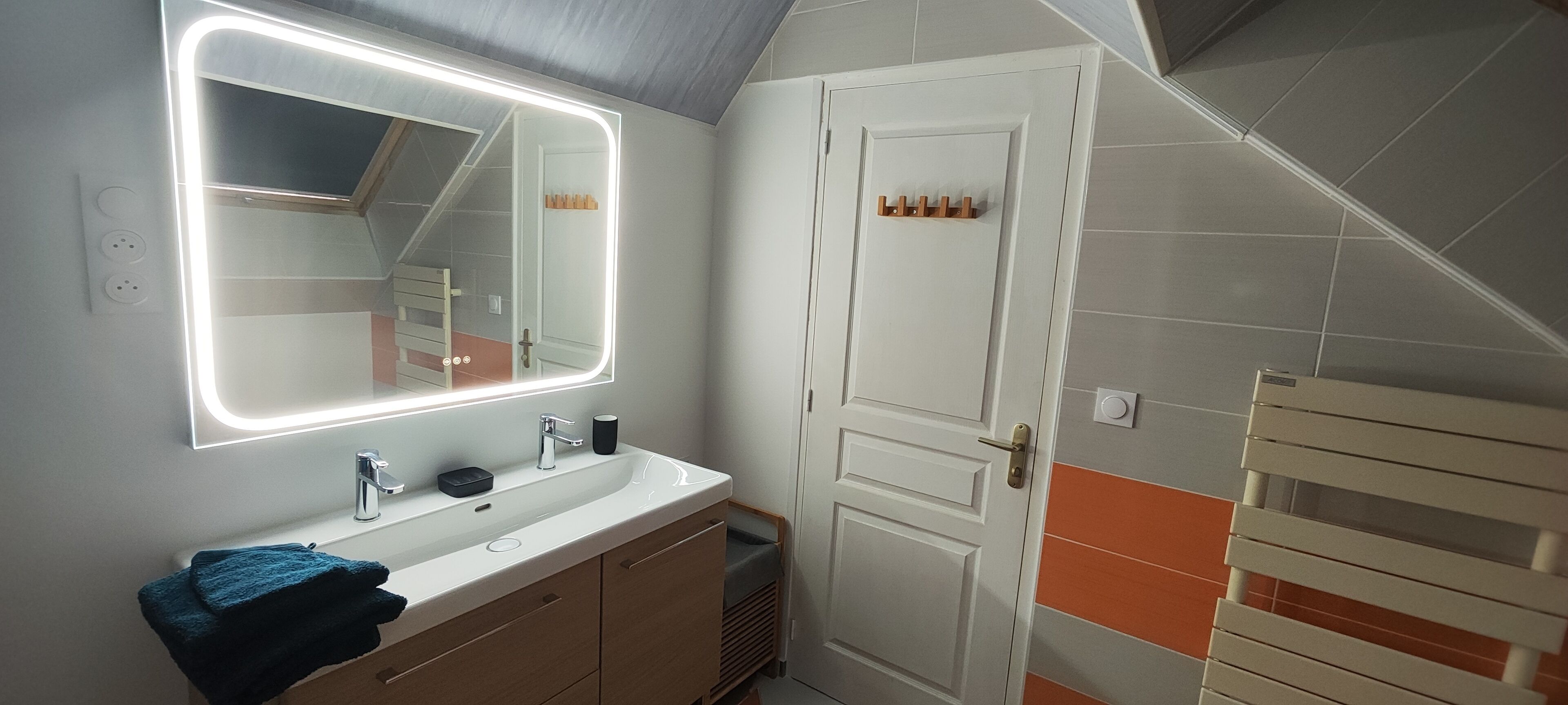 Une salle de bain avec un grand miroir, un lavabo et un porte-serviettes.