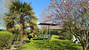 Un jardí ben cuidat amb una taula i cadires al pati, una barbacoa i una cadira hamaca.