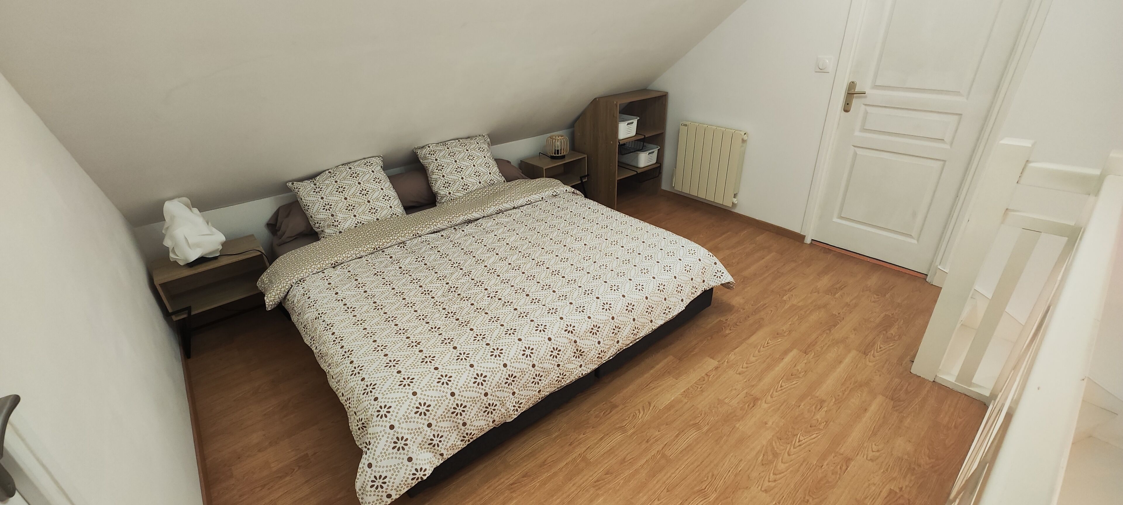 Ein Schlafzimmer mit Bett, Holzboden, weißen Wänden, einer Heizung und einer Tür.