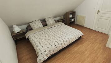 Ein Schlafzimmer mit Bett, Holzboden, weißen Wänden, einer Heizung und einer Tür.
